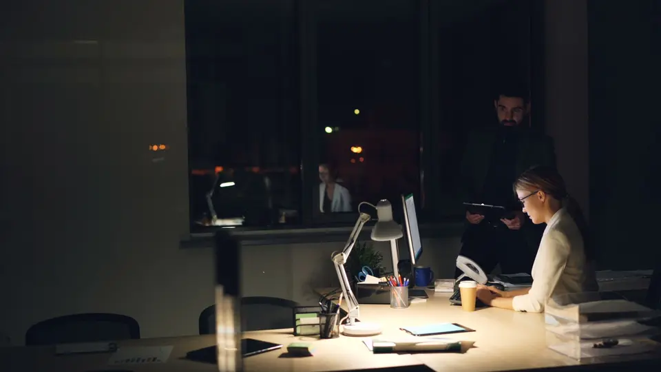 Open-plan startup bullpen with employees working late under exposed industrial pipes