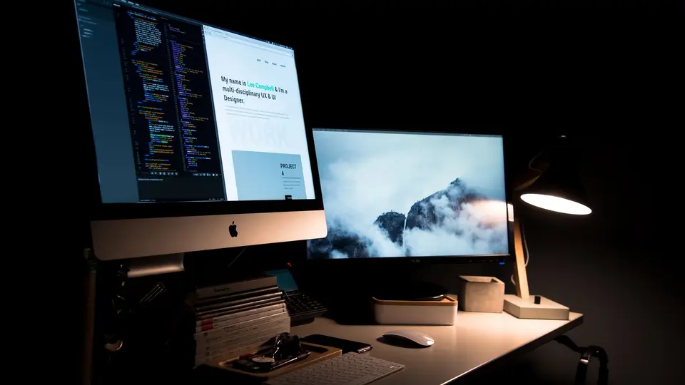 Minimalist desk with ultrawide curved monitor showing clean web application codebase
