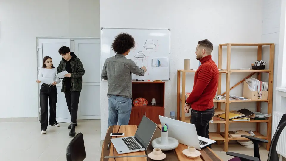 Open-plan startup bullpen with employees working late under exposed industrial pipes