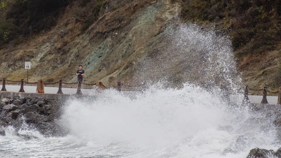 Solitary figure standing calmly on high ocean cliffs during a violent sea storm