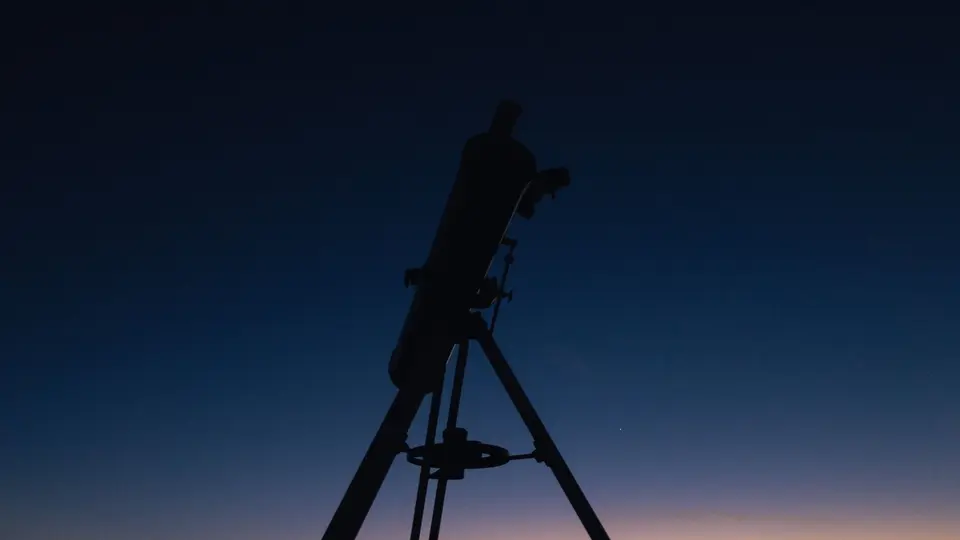 Astronomy telescope pointing at star-filled night sky with glowing milky way