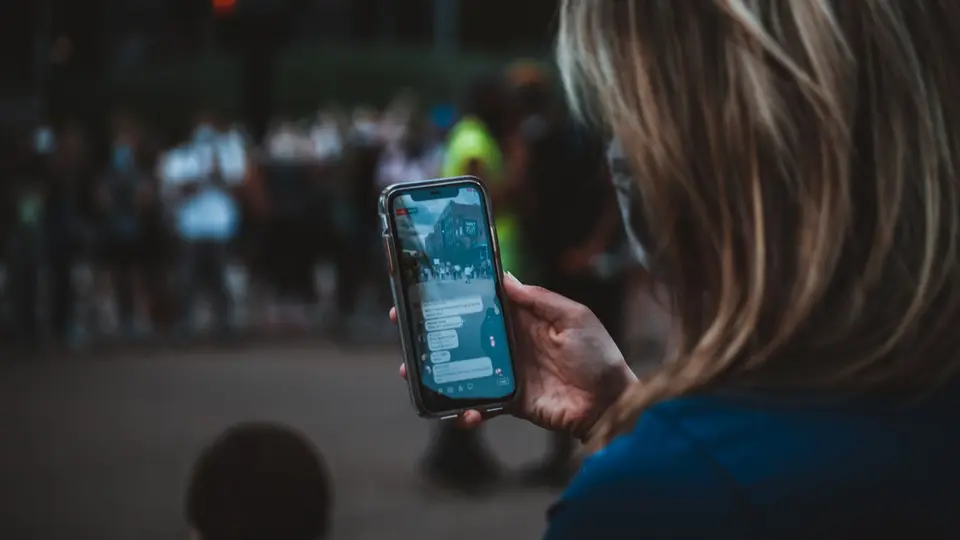 Smartphone with vertical video rig capturing breaking news surrounded by traditional news vans