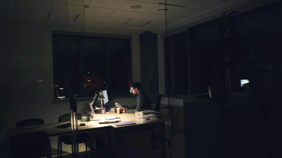 Silhouette of man in business casual working late at desk, monitor glow on face